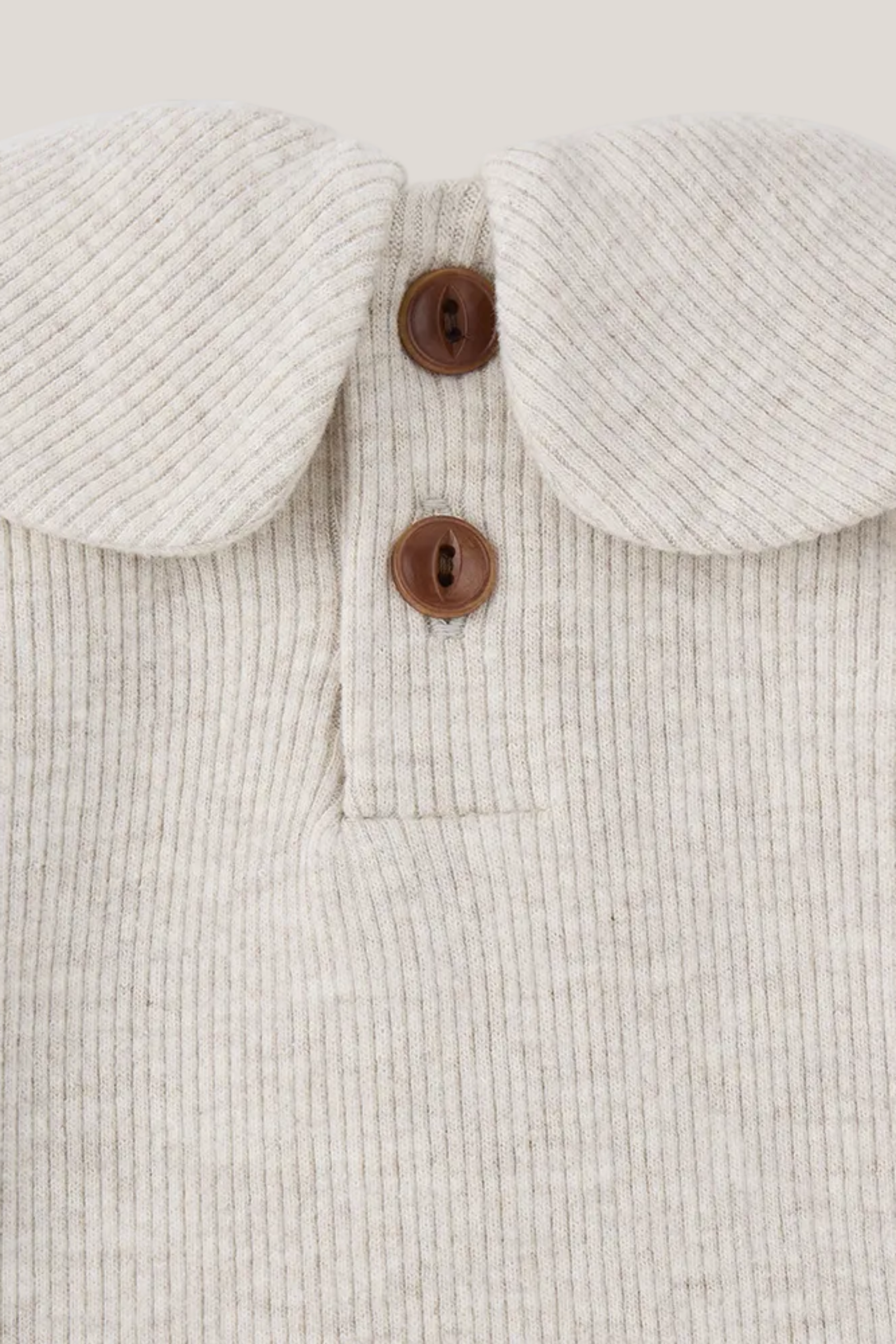Close-up of a beige corduroy garment with a collar and brown buttons on a white background