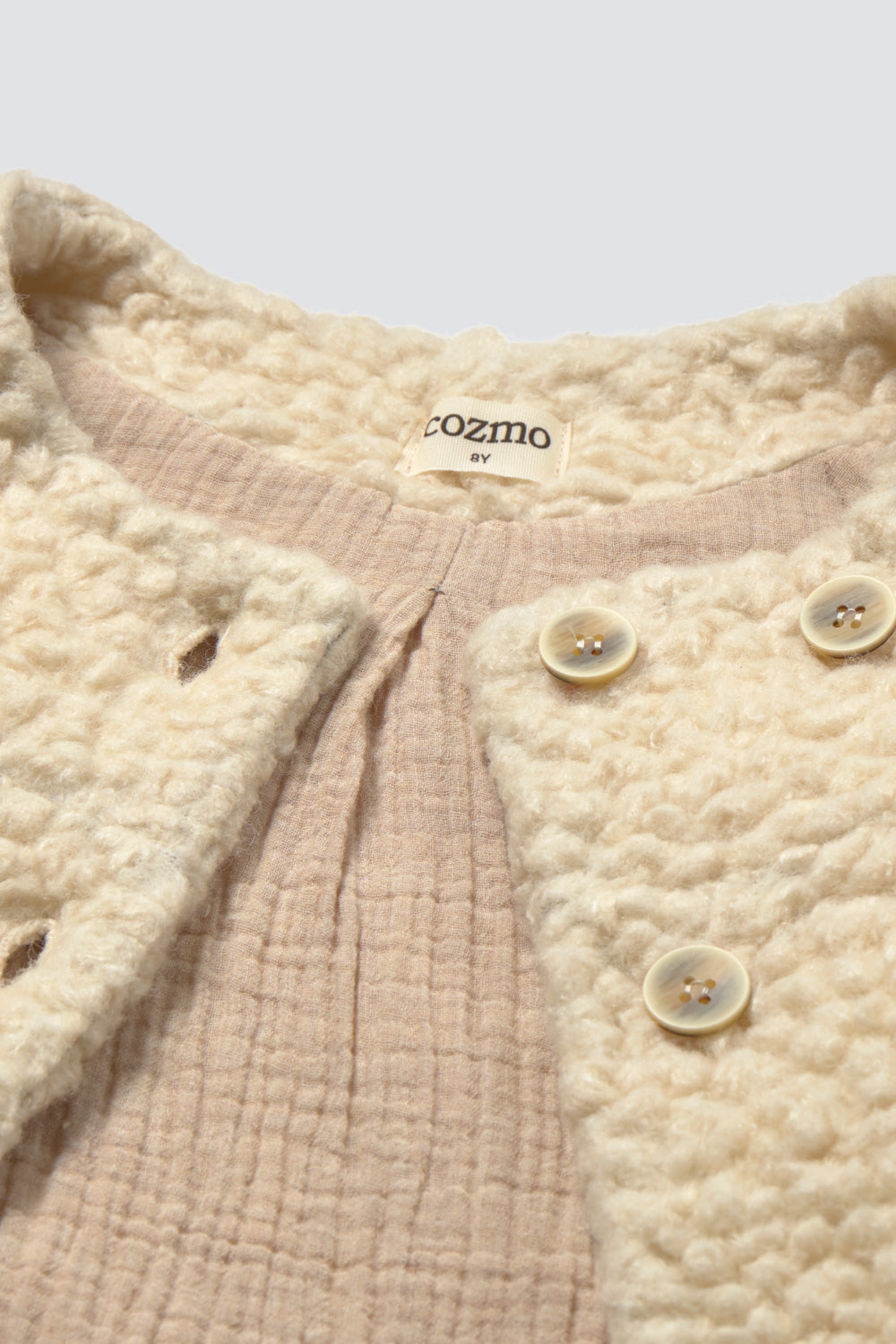 Close-up of a textured garment with buttons and a visible brand label on a light background