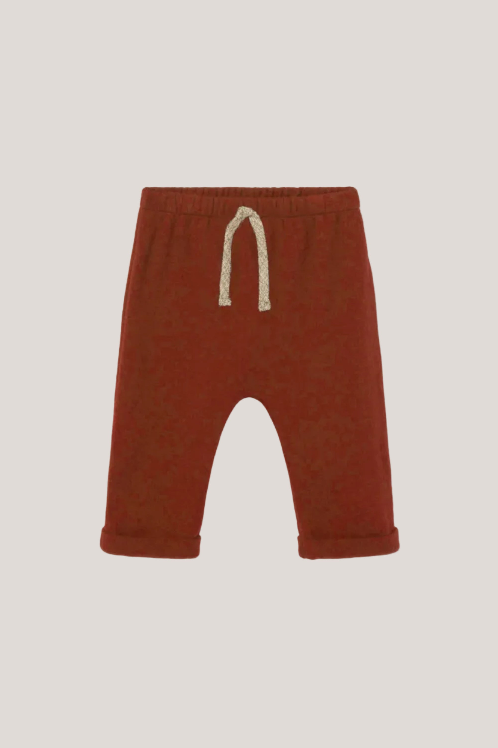 A pair of toddler knit pants in a rust red color, featuring a cream-colored drawstring at the elastic waistband, shown against a light gray background.