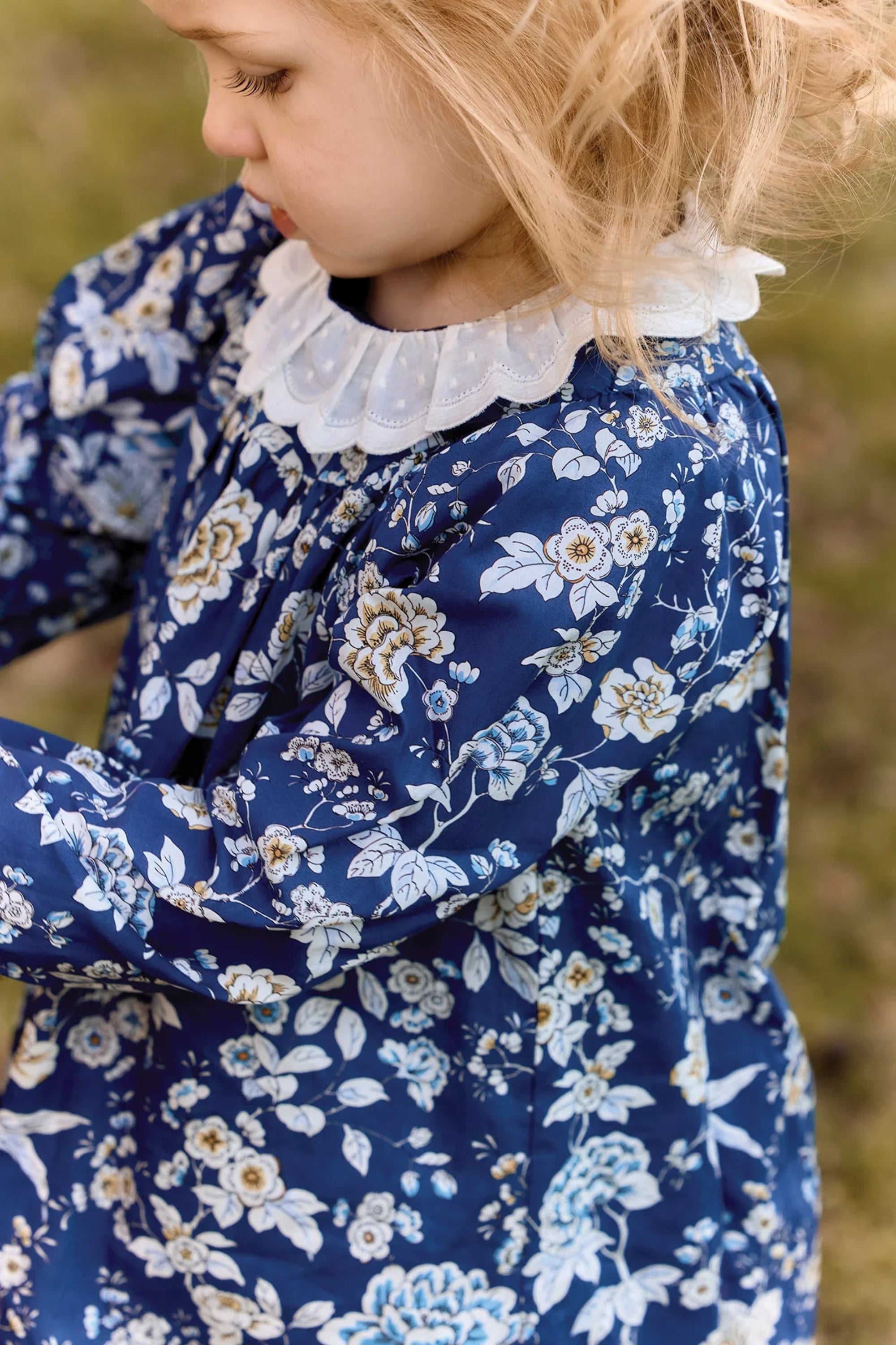 Child wearing a blue floral dress with a white collar against a natural background