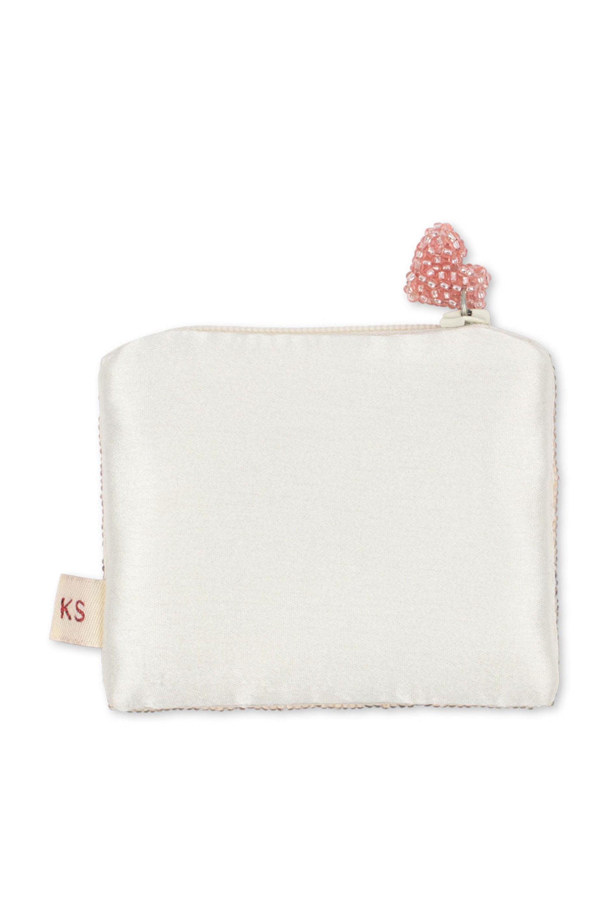 An off-white satin zippered pouch with a small pink beaded heart charm on the zipper pull and a small fabric tag on the side.