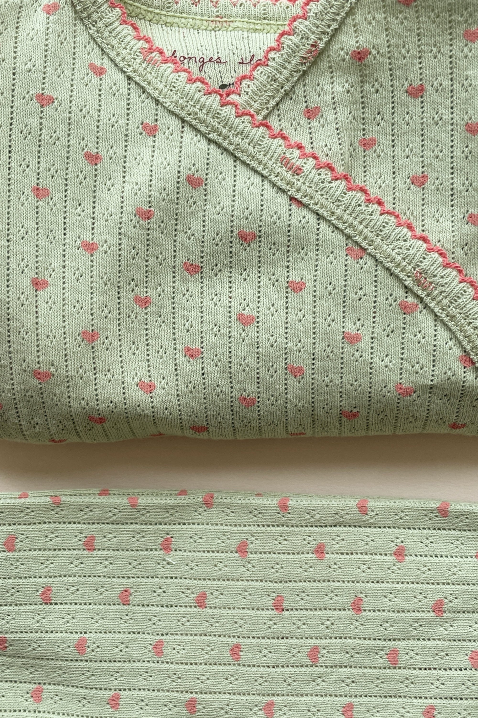 Close up of baby knit set in light green with hearts and pink detailing
