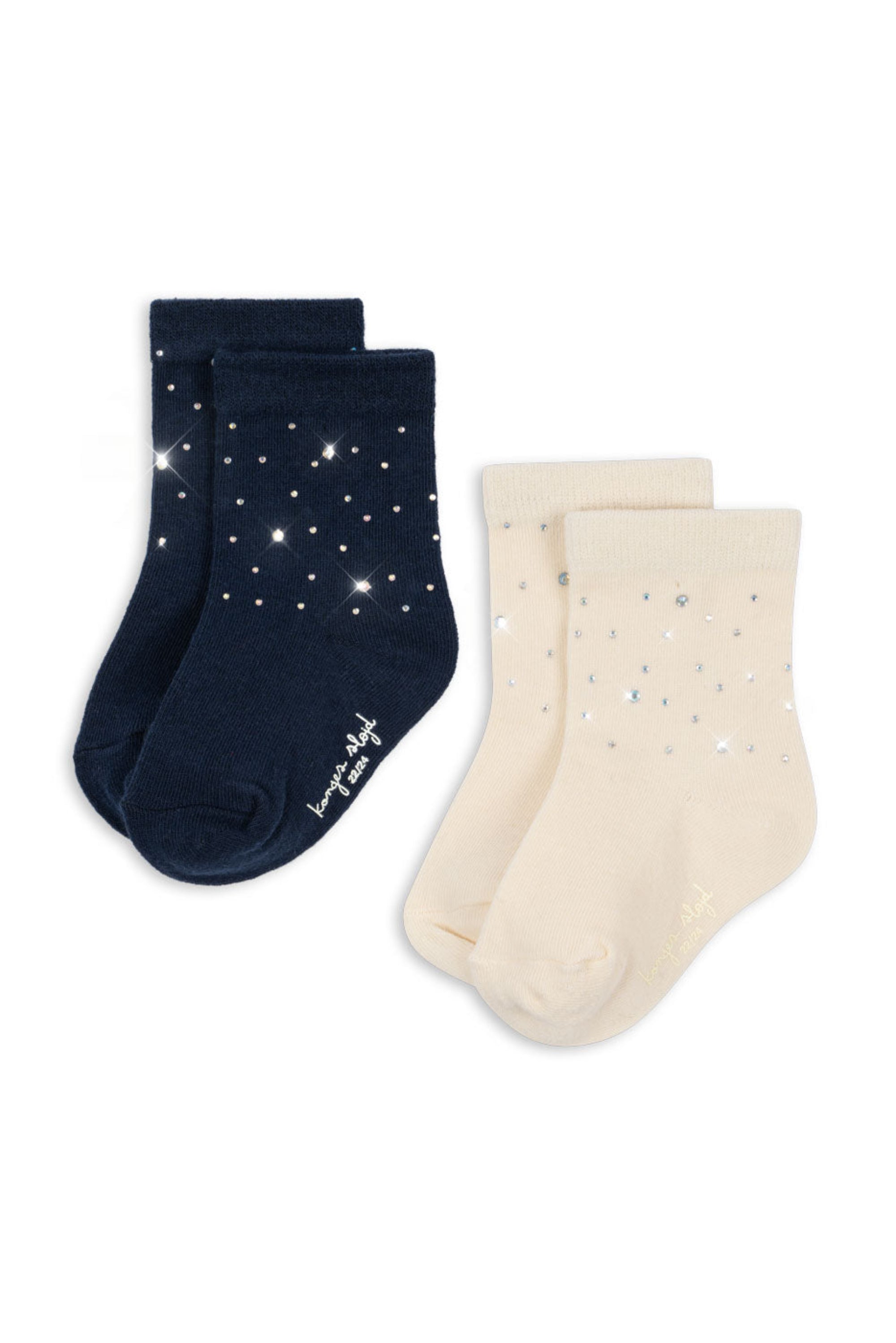 Two pairs of children's socks on a white background: one pair is navy blue with white star and sparkle prints, and the other pair is cream with matching star and sparkle prints.